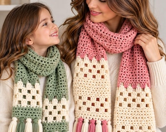 May include: Two crocheted scarves featuring a color-blocked design with a solid section, a square-patterned openwork section, and a fringe of alternating tassels. One scarf is sage green and cream, while the other is dusty rose and cream.