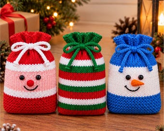 May include: Three knitted drawstring pouches featuring festive designs. The left pouch is red, white, and pink with a round red nose. The center pouch has red, white, and green stripes. The right pouch is blue and white with a carrot-shaped nose.