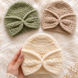 Puede incluir: Tres gorros de ganchillo en verde salvia, beige y crema. Cada gorro presenta un patrón de puntos texturizados y un detalle prominente en forma de lazo plegado en el borde delantero, creando una apariencia estructurada y superpuesta.