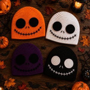 May include: Four crochet beanies featuring stitched facial expressions. The top left is orange with black eyes and mouth, the top right is white with black features, the bottom left is purple with black features, and the bottom right is black with white features.