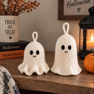 May include: Two off-white crocheted ghost ornaments with black yarn eyes and a small stitched smile. Each ghost features a loop at the top for hanging and a flared, wavy bottom edge. The ghosts are crafted from a textured yarn in a knit-like pattern.