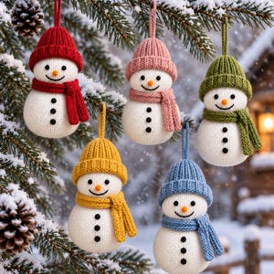 May include: Five knitted snowman ornaments hanging from a pine branch. Each snowman has a white body with three black buttons, an orange nose, and a matching colored hat and scarf in red, pink, green, yellow, or blue with a hanging loop.