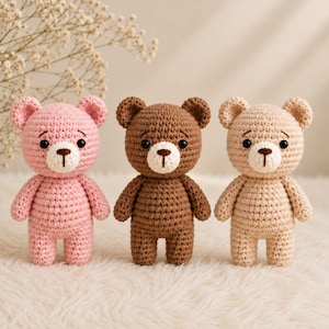 Könnte beinhalten: Drei handgefertigte Häkel-Teddybären in einer Reihe. Der Bär links ist hellrosa, der mittlere Bär ist dunkelbraun und der Bär rechts ist beige. Jeder Bär hat schwarze Kunststoffaugen, eine gestickte braune Nase und kleine Ohren.