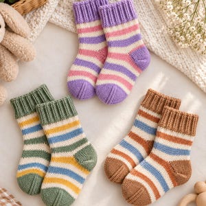 Peut inclure: Trois paires de chaussettes tricotées pour bébé à rayures horizontales. Une paire est violette, rose et blanche ; une paire est verte, jaune et bleue ; et une paire est marron, bleue et blanche. Chaque paire a un revers côtelé et un bout renforcé.