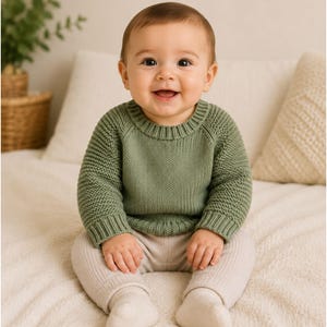 Può includere: Un maglione in maglia a maniche lunghe color verde salvia con girocollo e polsini a coste, abbinato a leggings in maglia a coste color beige chiaro. Il maglione presenta un motivo a maglia testurizzato sulle maniche e una finitura liscia.
