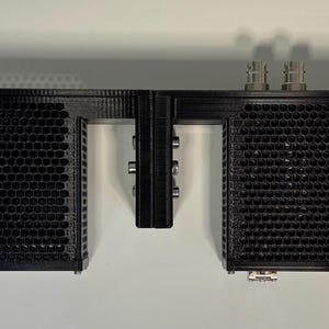 May include: A black electronic component with multiple rectangular sections. The sections have a perforated design. The component has several connectors and is mounted on a black frame. The item is designed for electronic equipment.