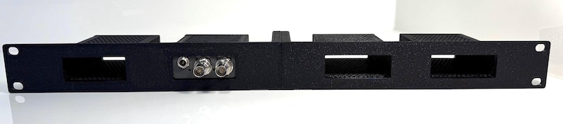 May include: A black metal rack mount panel with four rectangular openings and two circular connectors. The panel has mounting holes on each end and a textured surface.