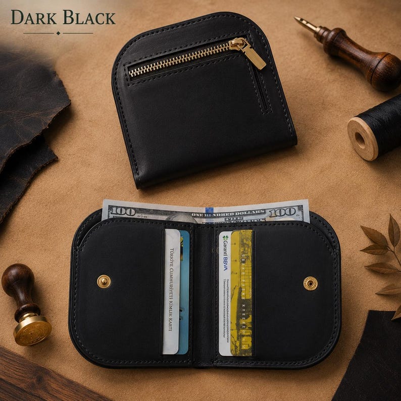 May include: A black leather wallet with a rounded top edge and a gold-tone metal zipper pocket on the exterior. The interior features card slots containing identification cards and a compartment holding a one hundred dollar bill.