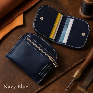 May include: A navy blue leather wallet with rounded edges and white stitching. One side features a metal zipper pocket, while the open side reveals internal card slots holding a yellow card and a white card. The text Navy Blue is visible.