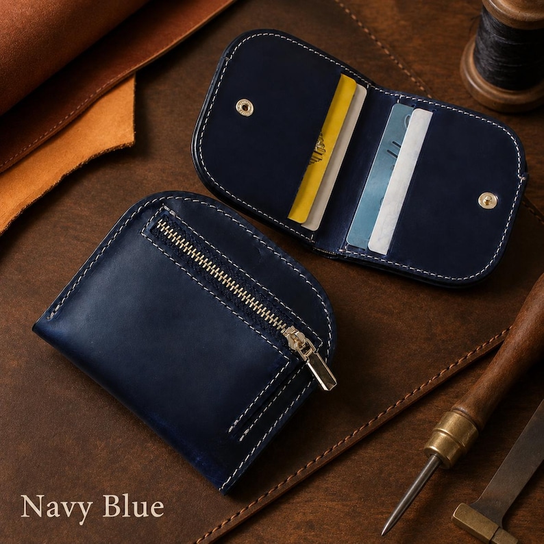 May include: A navy blue leather wallet with rounded edges and white stitching. One side features a metal zipper pocket, while the open side reveals internal card slots holding a yellow card and a white card. The text Navy Blue is visible.