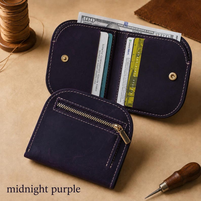 May include: A midnight purple leather wallet featuring a zippered exterior pocket, white contrast stitching, and an open interior with card slots and a currency compartment holding a one hundred dollar bill and various identification cards.