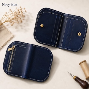 May include: A navy blue leather bifold wallet featuring rounded corners, white contrast stitching, and a gold-tone metal zipper on the exterior. The interior includes multiple card slots and a gold-tone snap button closure for secure storage.