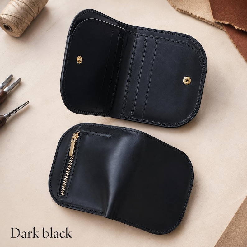 May include: A dark black leather wallet shown in two views. One view displays the open interior with multiple card slots and a gold-toned snap button closure. The other view shows the closed exterior featuring a vertical gold-toned metal zipper.