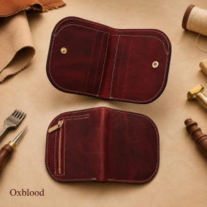 May include: An oxblood leather wallet shown in two views. The top view shows the open interior with card slots and two gold-tone snap buttons. The bottom view shows the closed exterior with a vertical gold-tone zipper pocket and white stitching.