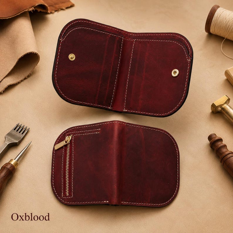 May include: An oxblood leather wallet shown in two views. The top view shows the open interior with card slots and two gold-tone snap buttons. The bottom view shows the closed exterior with a vertical gold-tone zipper pocket and white stitching.