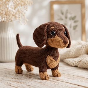 Könnte beinhalten: Gehäkelte Dackel-Hundefigur in Braun- und Beigetönen. Der handgefertigte Hund hat große, dunkle Augen und Schlappohren. Der Hund steht auf einer hellen Holzoberfläche.