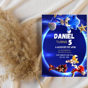 May include: A birthday party invitation featuring the character Sonic the Hedgehog. The invitation is blue with the text "DANIEL TURNS 5" and event details. The design includes images of Sonic and other characters.
