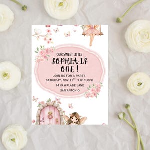 May include: A pink and white invitation for a first birthday party. The invitation features the text "OUR SWEET LITTLE SOPHIA IS ONE!" surrounded by floral and fairy illustrations. Additional text includes party details.