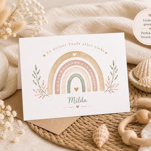 May include: A greeting card with a watercolor rainbow design in pastel colors, with the name "Milda" below. The card is on a brown envelope, with a vase of dried flowers and a wooden toy in the background.