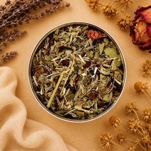 May include: A stainless steel bowl filled with a mix of dried herbs and flowers, including lavender and rose petals. The bowl sits on a tan surface, surrounded by dried flowers and a sprig of lavender.