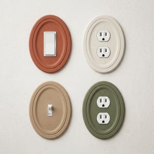 May include: Four oval-shaped wall plates featuring a matte finish in terracotta, cream, beige, and sage green. The set includes two white rocker and toggle light switches and two white dual electrical outlets, each centered within the oval frames.