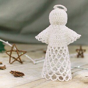 May include: A white crocheted angel ornament with a halo. The angel is standing on a wooden surface.