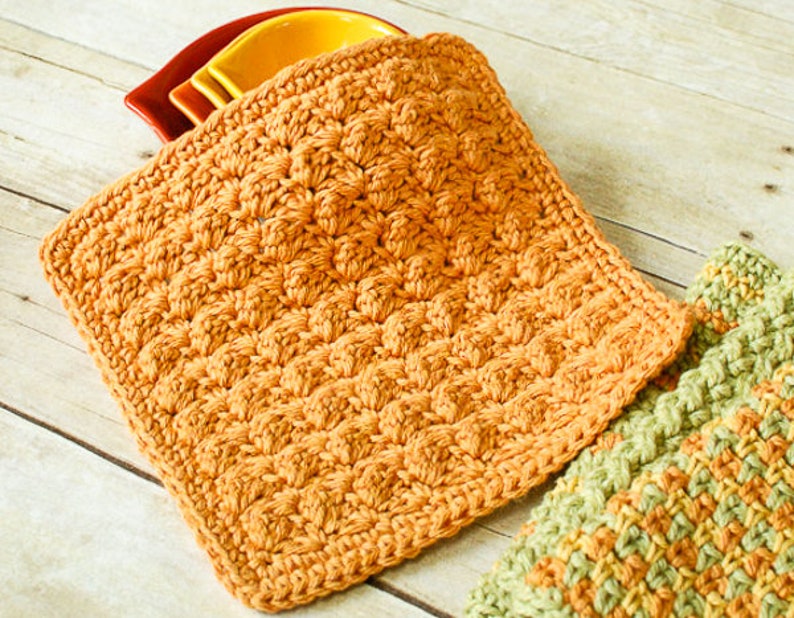 May include: A crocheted pot holder in a warm orange color. The pot holder is made with a textured stitch that creates a raised pattern.
