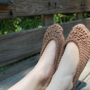 May include: A pair of brown knitted slippers with a textured design. The slippers are worn on a person's feet.