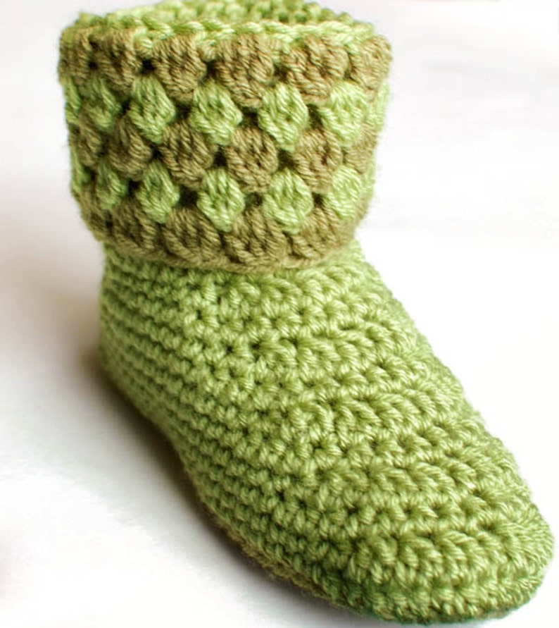 May include: Green crocheted slippers with a brown crocheted cuff. The slippers are made with a simple stitch pattern.