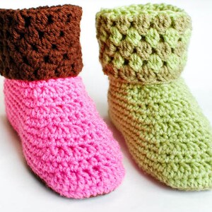 May include: Two pairs of crocheted slipper socks. One pair is pink with a brown cuff, and the other pair is green with a brown cuff.