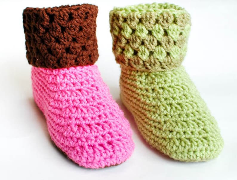 May include: Two pairs of crocheted slipper socks. One pair is pink with a brown cuff, and the other pair is green with a brown cuff.