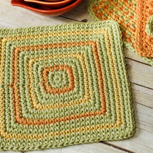 May include: Green, yellow, and orange crocheted square pot holder. The pot holder has a square shape with a smaller square in the center.