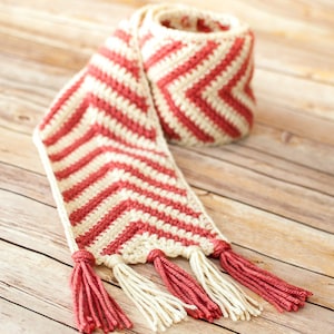 May include: A crocheted scarf with a chevron pattern in cream and coral with tassels on the ends.