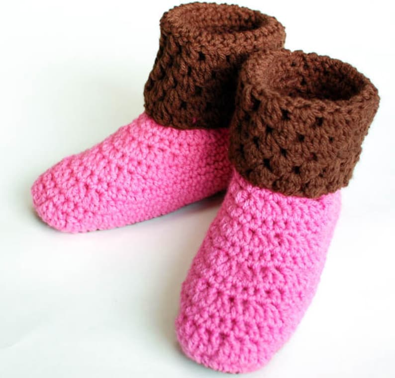 May include: A pair of pink and brown crocheted slippers with a brown cuff. The slippers are made with a simple stitch pattern and have a soft, cozy look.
