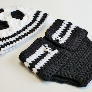 May include: A crocheted soccer-themed baby set, featuring a white and black soccer ball hat and matching leg warmers. The leg warmers are dark gray with white stripes and soccer ball buttons.