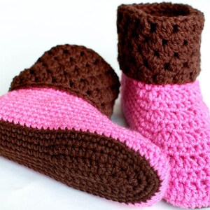 May include: A pair of crocheted slippers with a brown and pink color scheme. The slippers have a brown cuff and a pink sole.