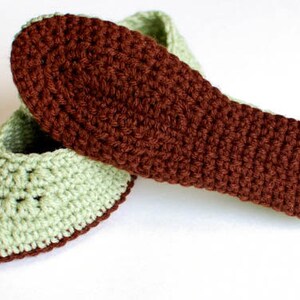 May include: A pair of crocheted slippers in green and brown. The slippers are made with a simple stitch pattern and have a rounded toe.