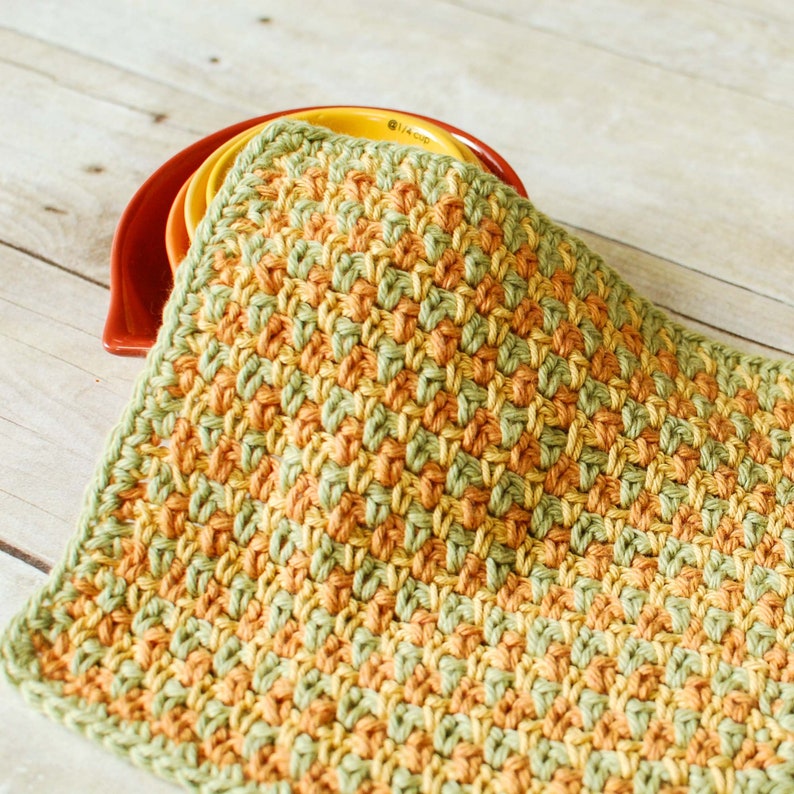 May include: A crocheted dishcloth in a green and orange color pattern. The dishcloth is made with a simple stitch and has a textured look.