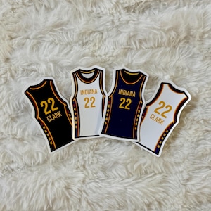 May include: Four die-cut stickers of basketball jerseys. Two are white and gold, one is navy and gold, and one is black and gold. Each jersey has the number 22 on it. Two say "Clark" and two say "Indiana".
