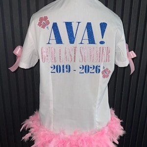 May include: White shirt with pink feather trim and bows. The back displays "AVA!" in blue glitter, with "OUR LAST SUMMER 2019-2026" in pink, and pink floral details. A fun, celebratory garment.