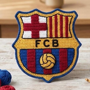以下が含まれることがあります： 赤、黄、青、白の糸で編まれたFCバルセロナのエンブレムのクロッシェ編み。盾の形をしたデザインで、中央には黒い文字でFCB、赤い十字、縦縞模様、そして中央に黄色いサッカーボールが配置されています。