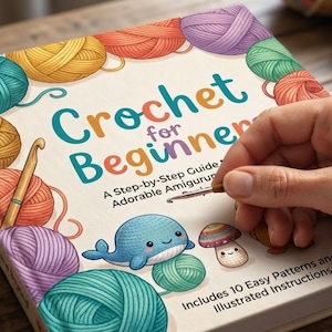 Könnte beinhalten: Ein Softcover-Buch mit dem Titel Crochet for Beginners: A Step-by-Step Guide to Adorable Amigurumi. Das Cover zeigt bunte Wollknäuel, eine Häkelnadel, einen blauen Wal und einen Pilz sowie den Hinweis auf 10 enthaltene einfache Anleitungen.