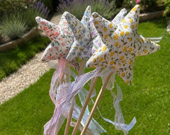 May include: A set of four fabric star-shaped wands attached to wooden dowels. Each star features a different floral print in yellow, blue, pink, and purple. Long, thin, translucent ribbons in matching pastel colors are tied to the base of each star.