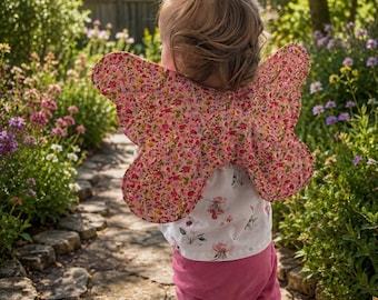 May include: A pair of fabric butterfly wings featuring a small-scale floral pattern in shades of pink, red, and green. The wings are attached to a white short-sleeved top with a delicate floral print, paired with solid dark pink leggings.