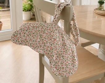 May include: A fabric bag featuring a white base with a repeating pattern of small pink flowers and green leaves. The bag has a distinct curved shape and a gathered, scrunchie-style handle made from the same floral fabric, providing a soft texture.