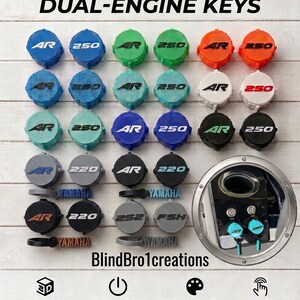 May include: A collection of circular, 3D-printed dual-engine key covers in various colors, featuring embossed text like AR, 250, 220, 252, FSH, and YAMAHA. The image includes the text CUSTOMIZE YOUR DUAL-ENGINE KEYS and BlindBro1creations.