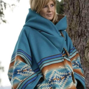 May include: A hooded coat in a vibrant turquoise blue featuring a prominent geometric pattern in shades of brown, cream, and dark blue. The garment includes a large, structured hood and wooden toggle closures along the front opening.