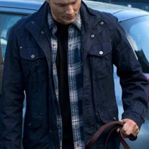 Könnte beinhalten: Eine dunkelmarineblaue Utility-Jacke mit hohem Kragen, mehreren aufgesetzten Vordertaschen mit silberfarbenen Druckknöpfen und einem durchgehenden Reißverschluss, getragen über einem schwarzen Hemd und einem blau-weiß-roten karierten Hemd.