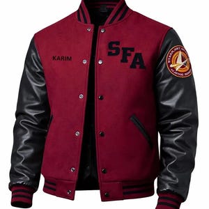 Op de afbeelding: Een bordeauxrode varsity-jas met zwarte mouwen, voorzien van de tekst "KARIM" op de rechterborst en "SFA" op de linkerborst. Een cirkelvormig embleem bevindt zich op de linkerschouder. De jas heeft een drukknoopsluiting, een geribbelde kraag en boorden.
