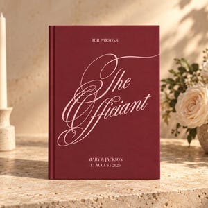 May include: A deep red hardcover book with white text that reads BOB PARSONS, The Officiant, MARY & JACKSON, and 17 AUGUST 2026. The cover features elegant, flowing script lettering for the title and clean, sans-serif font for the other details.